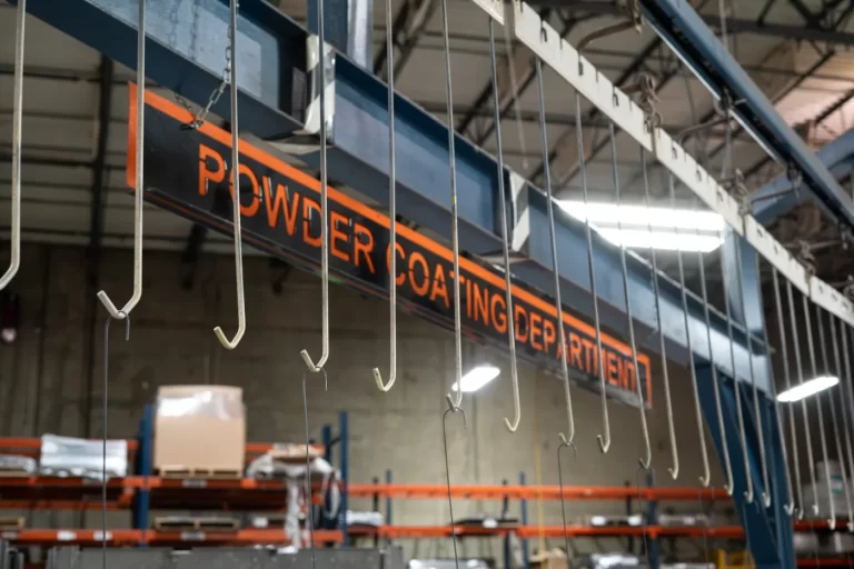 Overhead conveyor hooks on SPM’s powder coating line, below the Powder Coating Department sign